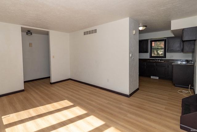 unfurnished living room featuring a textured ceiling, a sink, light wood-style flooring, and baseboards