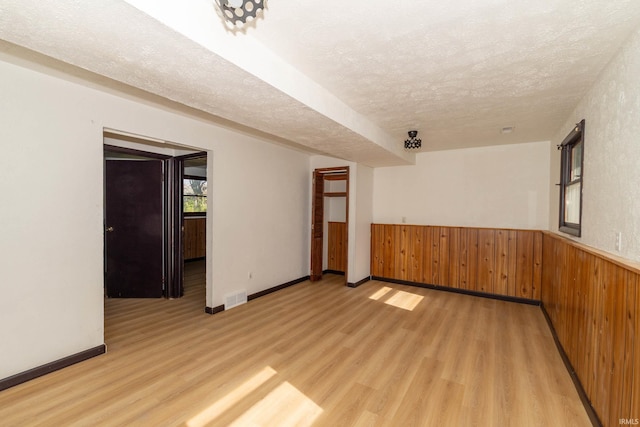 spare room with a textured ceiling, light wood finished floors, wainscoting, wood walls, and baseboards