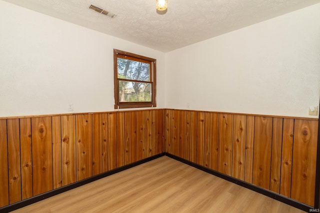 spare room featuring light wood-type flooring, wainscoting, wood walls, and a textured ceiling