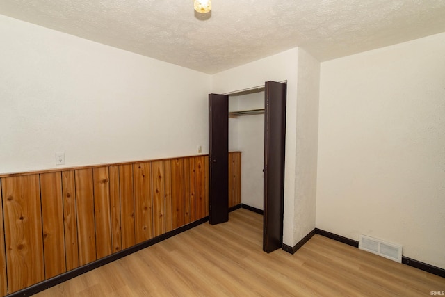 spare room featuring light wood-style flooring, a textured ceiling, and baseboards