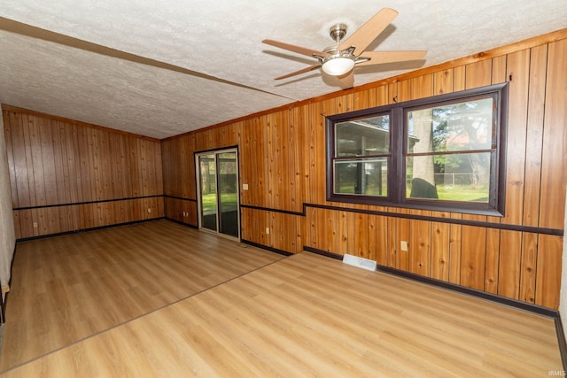 spare room featuring light wood-type flooring, ceiling fan, a textured ceiling, wooden walls, and baseboards