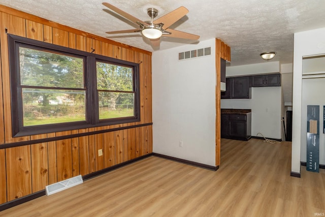 unfurnished room featuring plenty of natural light, wooden walls, baseboards, light wood-type flooring, and a ceiling fan