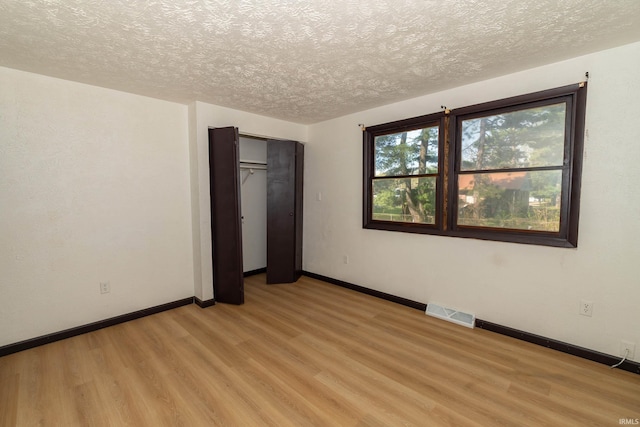 unfurnished bedroom with light wood-type flooring, a textured ceiling, baseboards, and a closet