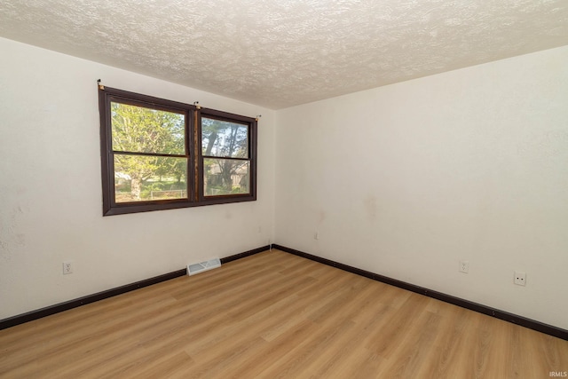 spare room with light wood finished floors, a textured ceiling, and baseboards