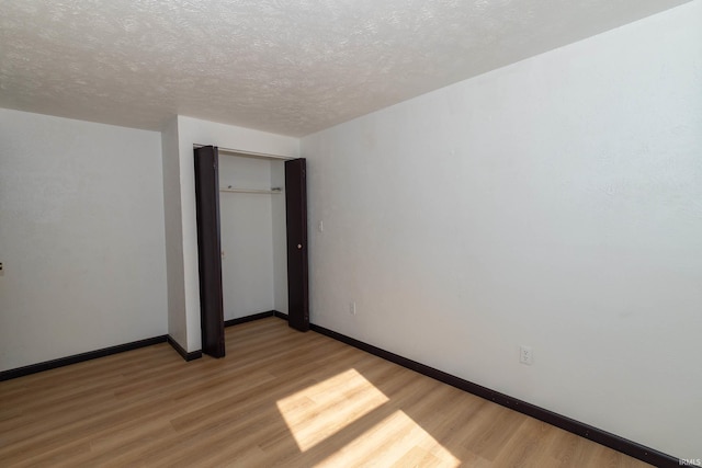 unfurnished bedroom with light wood finished floors, a textured ceiling, a closet, and baseboards
