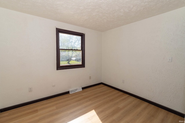spare room featuring light wood-style flooring, a textured ceiling, and baseboards