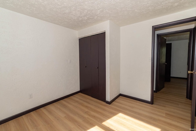 empty room with light wood finished floors, a textured ceiling, and baseboards