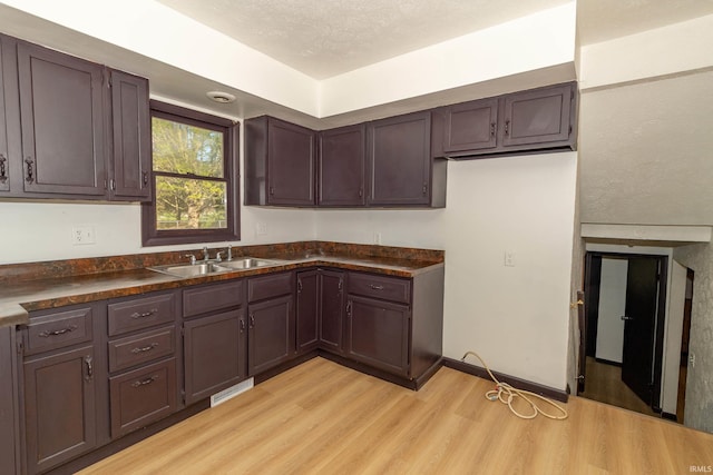 kitchen with a sink, dark countertops, light wood finished floors, and dark brown cabinets