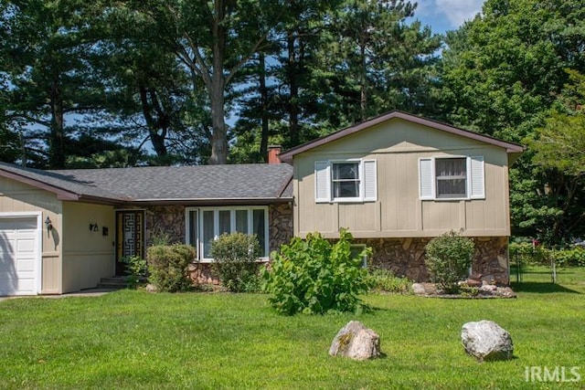 tri-level home featuring stone siding, an attached garage, and a front yard
