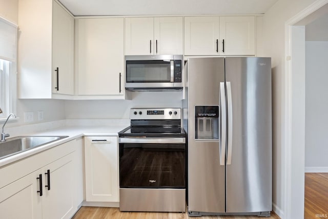 1425 Adams St, Lafayette, IN 47905 - kitchen featuring appliances with stainless steel finishes, white cabinets, light countertops, light wood-type flooring, and a sink