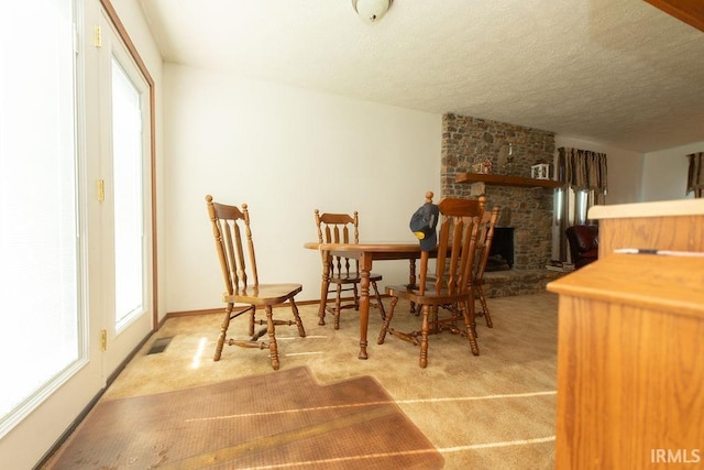 dining area featuring carpet flooring, a textured ceiling, and a large fireplace