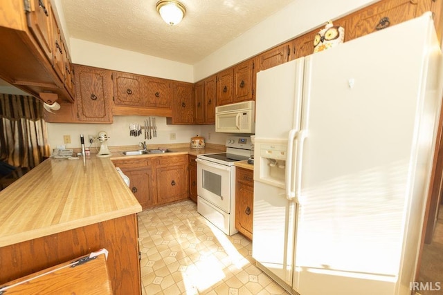 kitchen featuring white appliances, brown cabinetry, a sink, light tile patterned floors, and a textured ceiling