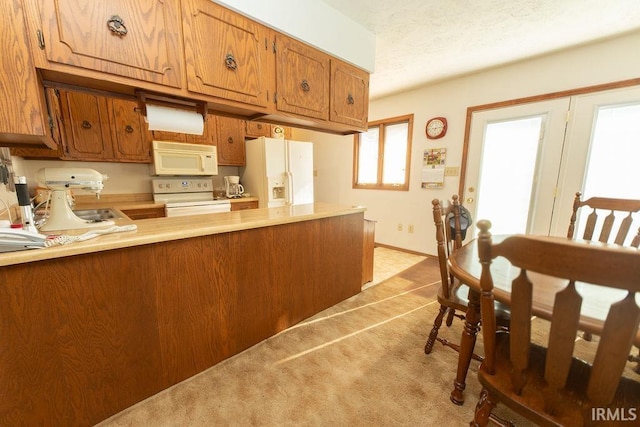 kitchen featuring white appliances, light countertops, brown cabinetry, a peninsula, and light colored carpet