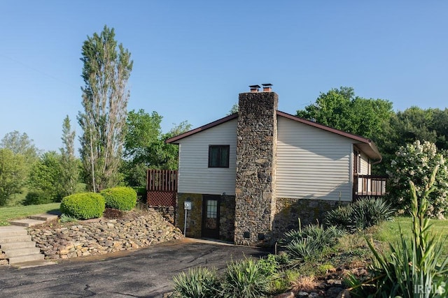 view of side of home with stone siding, a chimney, a wooden deck, and driveway