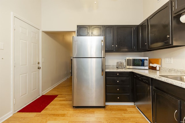kitchen with stainless steel appliances, light wood finished floors, baseboards, and light stone countertops