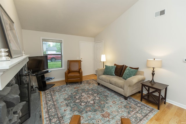 living room featuring wood finished floors, baseboards, high vaulted ceiling, and a fireplace