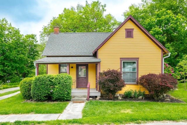 view of front of home featuring a chimney, a porch, a front yard, and a shingled roof
