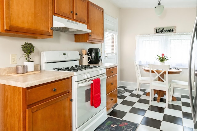 kitchen with white range with gas stovetop, under cabinet range hood, dark flooring, light countertops, and brown cabinetry