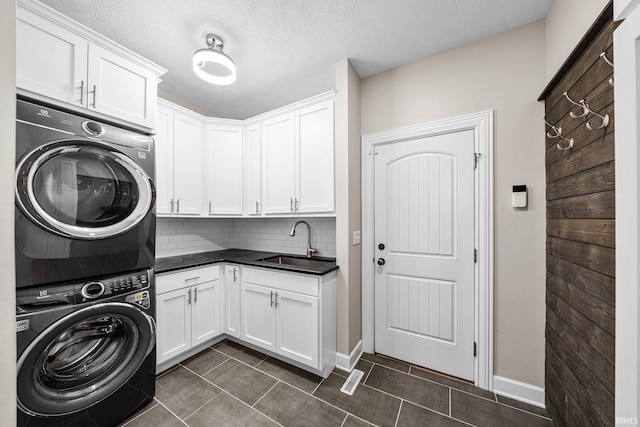 laundry area featuring stacked washer / dryer, cabinet space, dark tile patterned floors, a textured ceiling, and baseboards