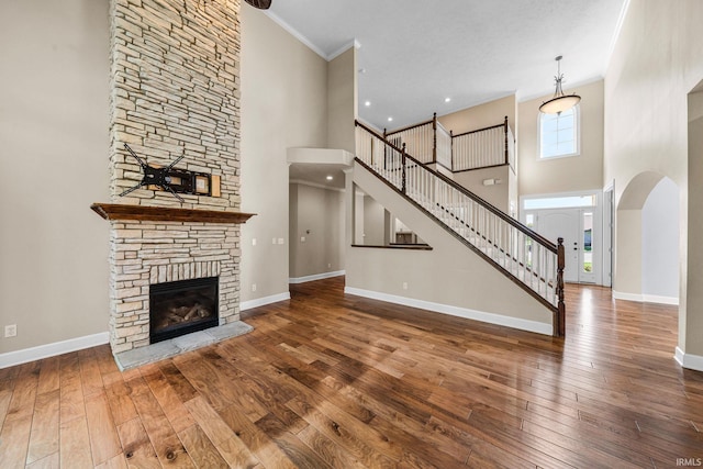 unfurnished living room with a high ceiling, ornamental molding, hardwood / wood-style flooring, a fireplace, and baseboards