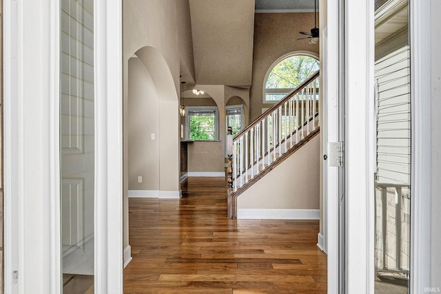 foyer featuring arched walkways, ceiling fan, wood finished floors, baseboards, and stairs