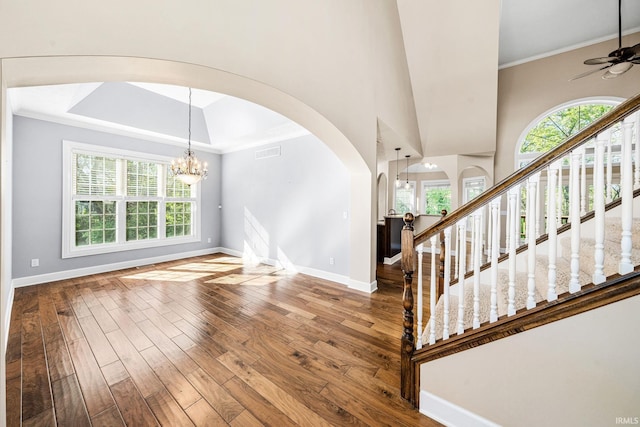 foyer with arched walkways, wood finished floors, baseboards, healthy amount of natural light, and crown molding