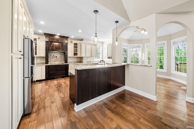 kitchen with premium range hood, wood-type flooring, glass insert cabinets, light stone counters, and recessed lighting