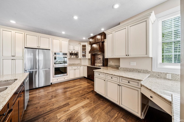 kitchen featuring appliances with stainless steel finishes, dark wood-style flooring, recessed lighting, light stone countertops, and custom range hood