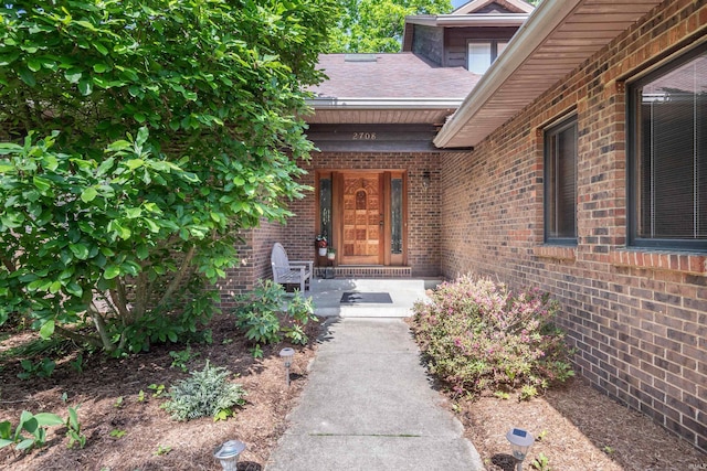 doorway to property with brick siding and roof with shingles