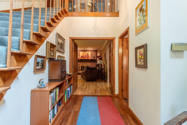 corridor with wood finished floors, a high ceiling, stairway, and a chandelier