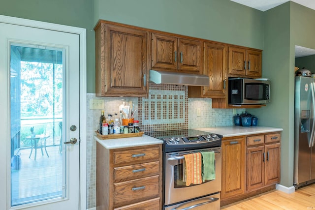 kitchen with appliances with stainless steel finishes, under cabinet range hood, brown cabinets, and tasteful backsplash