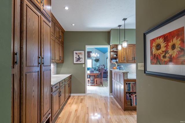 kitchen with backsplash, light wood finished floors, open shelves, brown cabinets, and decorative light fixtures