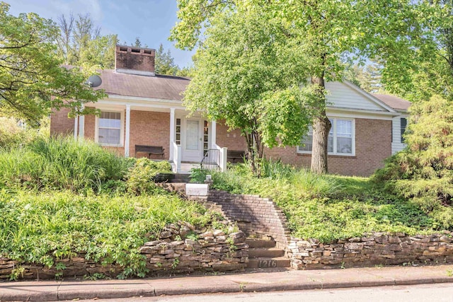 view of front of home featuring brick siding, a porch, and a chimney