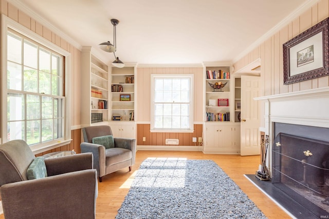 sitting room featuring crown molding, plenty of natural light, built in features, a fireplace, and light wood finished floors