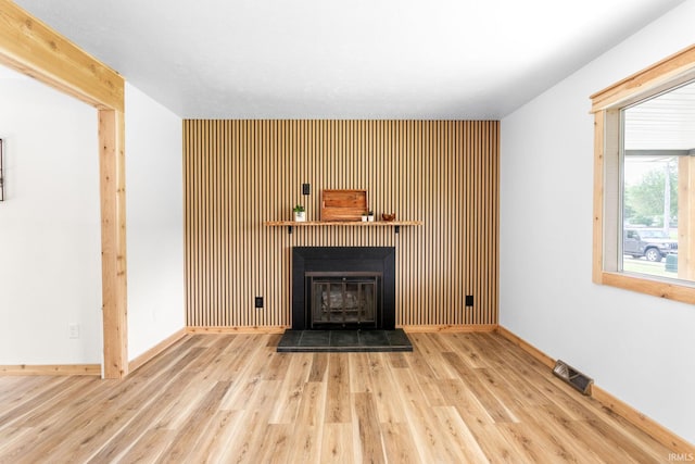unfurnished living room with wood finished floors, a fireplace with raised hearth, an accent wall, and baseboards