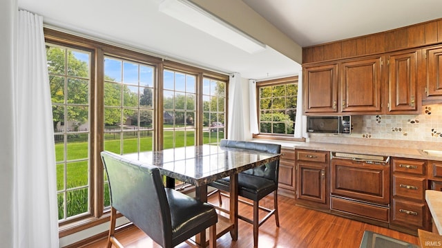 kitchen with light countertops, black microwave, decorative backsplash, dark wood-style flooring, and paneled dishwasher