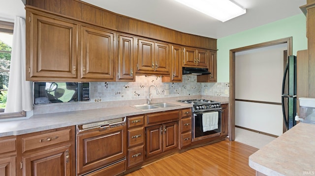 kitchen with a sink, black appliances, under cabinet range hood, light countertops, and tasteful backsplash