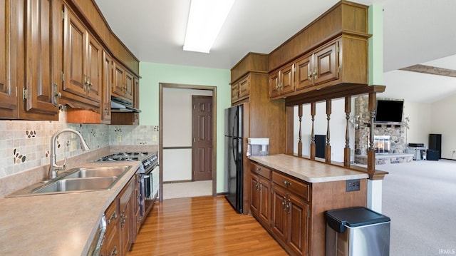 kitchen with gas stove, under cabinet range hood, freestanding refrigerator, backsplash, and a sink