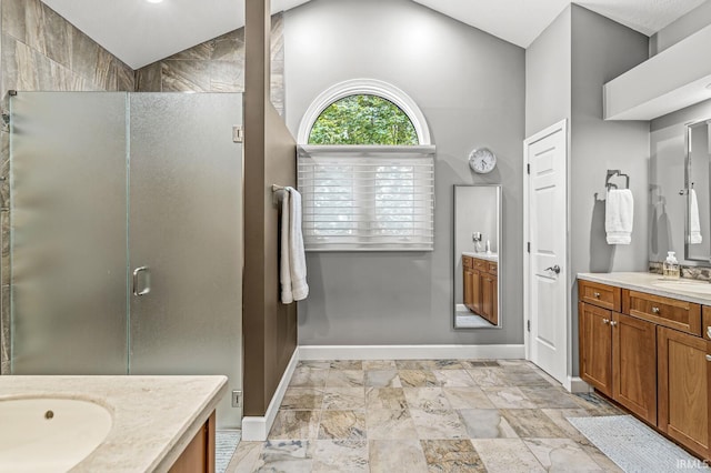 bathroom featuring a stall shower, two vanities, baseboards, and vaulted ceiling