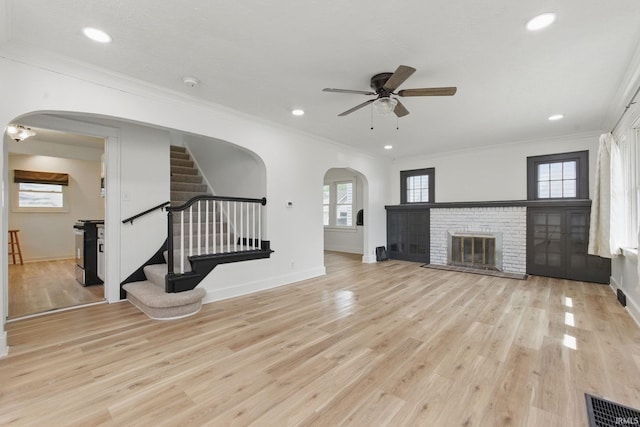 unfurnished living room featuring arched walkways, a ceiling fan, baseboards, light wood-type flooring, and crown molding