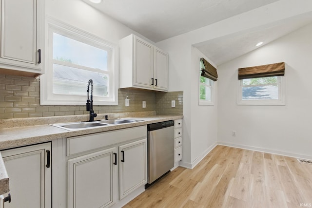 kitchen with dishwasher, a sink, vaulted ceiling, light wood-style floors, and decorative backsplash