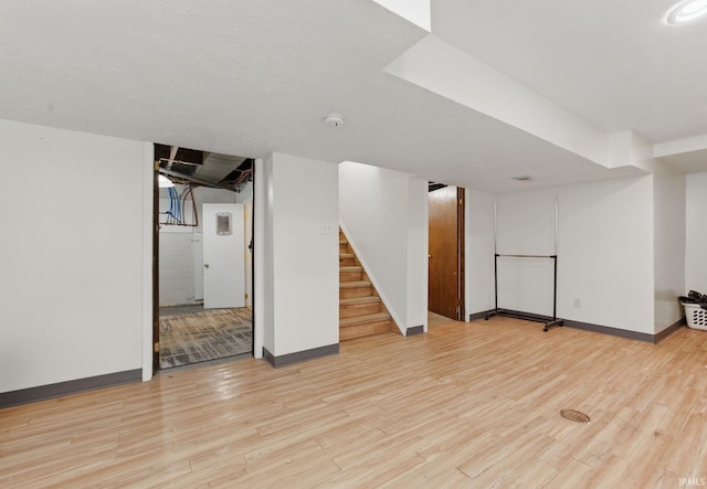 finished below grade area with baseboards, light wood-type flooring, and stairs