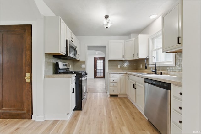 kitchen featuring appliances with stainless steel finishes, a sink, decorative backsplash, light wood finished floors, and light countertops