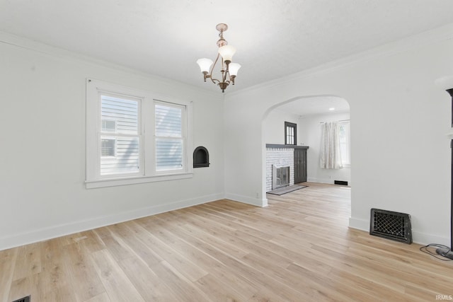 unfurnished living room featuring a brick fireplace, a chandelier, healthy amount of natural light, arched walkways, and ornamental molding