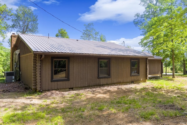 view of side of home with a chimney, metal roof, central AC, and log exterior