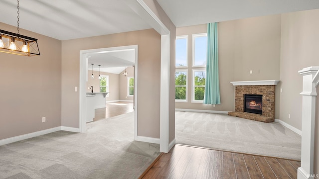 5937 Liam Ln, Fort Wayne, IN 46818 - unfurnished living room with wood finished floors, carpet flooring, a chandelier, a fireplace, and baseboards