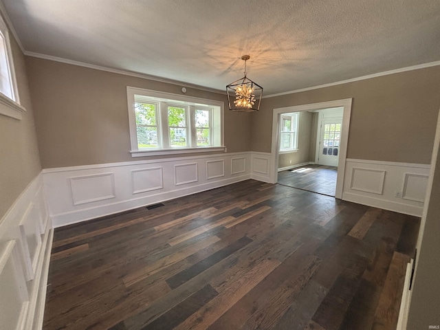 unfurnished dining area with a chandelier, ornamental molding, plenty of natural light, dark wood finished floors, and a decorative wall