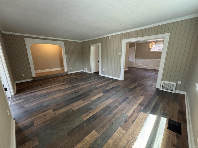 unfurnished room with ornamental molding, dark wood-style floors, a textured ceiling, arched walkways, and baseboards