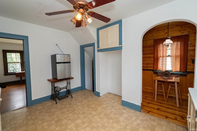 unfurnished living room featuring a ceiling fan, arched walkways, wood walls, and baseboards