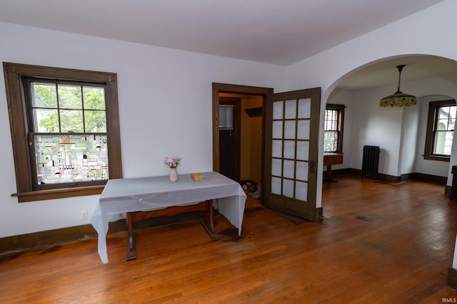 dining room featuring arched walkways, wood finished floors, radiator, and baseboards